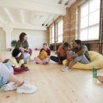 Group of young people sitting on the floor discussing new dance together in dance studio